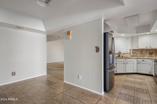 kitchen with sink, stainless steel fridge with ice dispenser, light tile patterned flooring, backsplash, and white cabinets