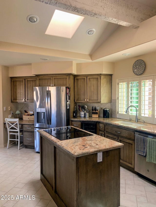 kitchen featuring sink, stainless steel appliances, a center island, light stone counters, and decorative backsplash