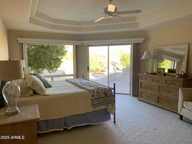 bedroom with a tray ceiling, light carpet, multiple windows, and access to outside