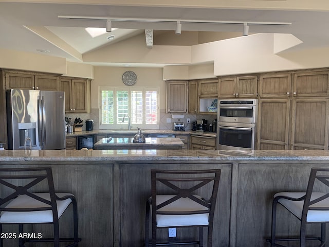 kitchen featuring appliances with stainless steel finishes, lofted ceiling, a kitchen bar, kitchen peninsula, and light stone countertops