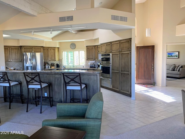 kitchen featuring a kitchen breakfast bar, kitchen peninsula, beamed ceiling, stainless steel appliances, and decorative backsplash