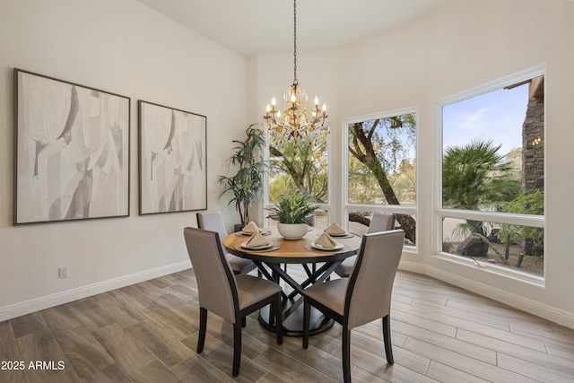 dining space with a notable chandelier, wood finished floors, a towering ceiling, and baseboards