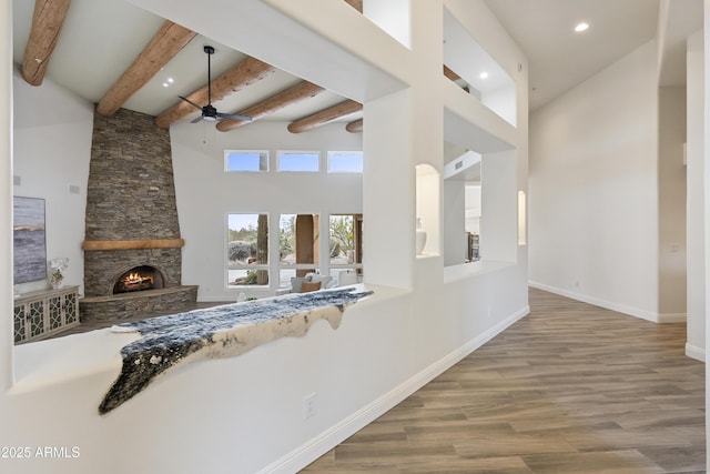 interior space featuring a high ceiling, ceiling fan, a stone fireplace, wood finished floors, and baseboards