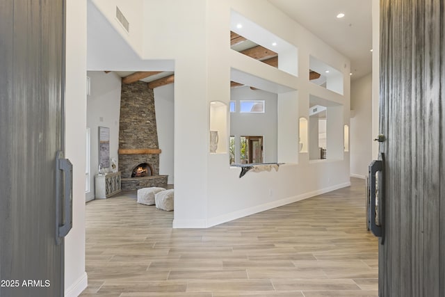 hallway featuring light wood-style floors, baseboards, visible vents, and a high ceiling