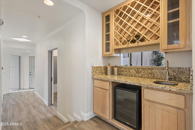 bar with beverage cooler, a sink, light wood-style floors, baseboards, and wet bar