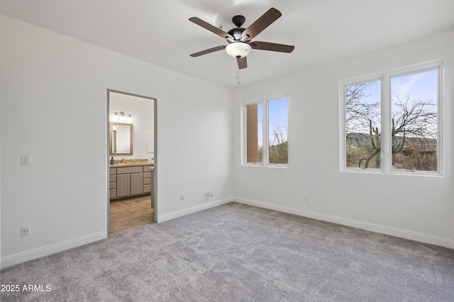 unfurnished bedroom with ceiling fan, connected bathroom, light carpet, a sink, and baseboards