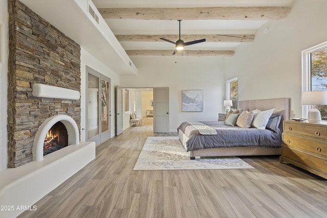 bedroom with light wood-style floors, visible vents, a fireplace, and beamed ceiling