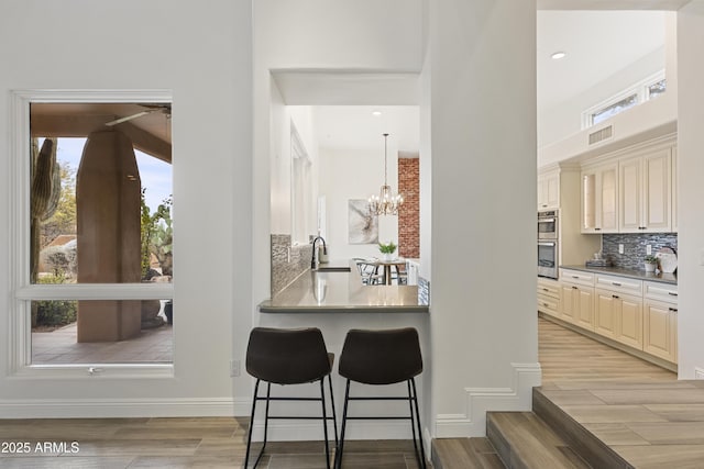 kitchen featuring a sink, light wood-style floors, double oven, a kitchen bar, and backsplash