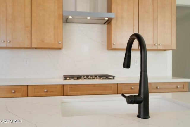 kitchen with light stone counters, backsplash, wall chimney range hood, and a sink