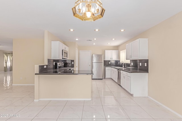 kitchen with a peninsula, white cabinetry, dark countertops, stainless steel appliances, and a sink