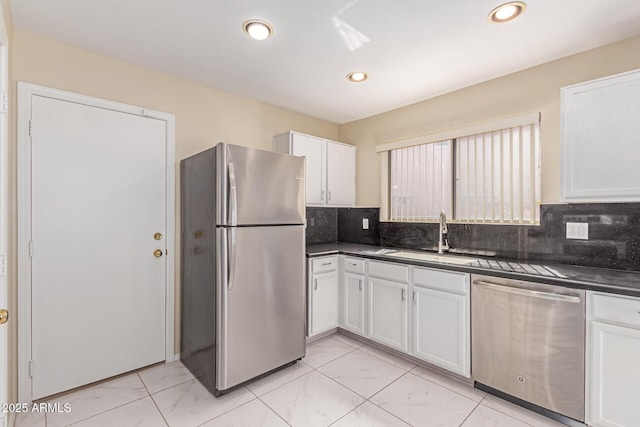 kitchen with appliances with stainless steel finishes, a sink, white cabinets, and dark countertops