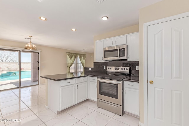 kitchen featuring white cabinets, dark countertops, a peninsula, and appliances with stainless steel finishes