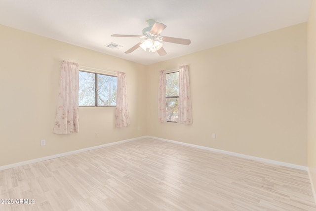 empty room featuring a wealth of natural light, light wood-style floors, visible vents, and baseboards
