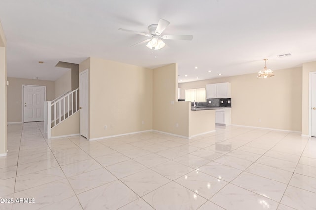 unfurnished living room with baseboards, stairs, and ceiling fan with notable chandelier