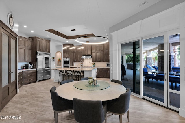 dining room featuring light hardwood / wood-style flooring, a healthy amount of sunlight, and a raised ceiling