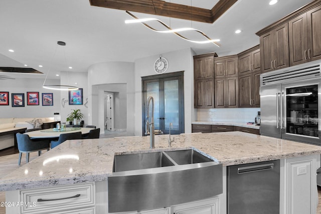 kitchen featuring a center island with sink, sink, light stone countertops, and decorative light fixtures