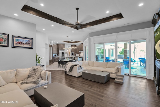 living room featuring dark wood-type flooring, ceiling fan, and a raised ceiling