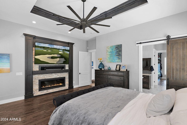 bedroom featuring hardwood / wood-style floors, ceiling fan, a barn door, and a stone fireplace