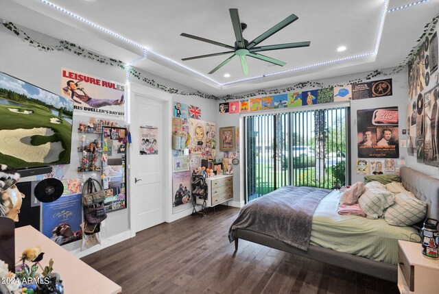 bedroom with ceiling fan, dark hardwood / wood-style floors, a tray ceiling, and access to outside