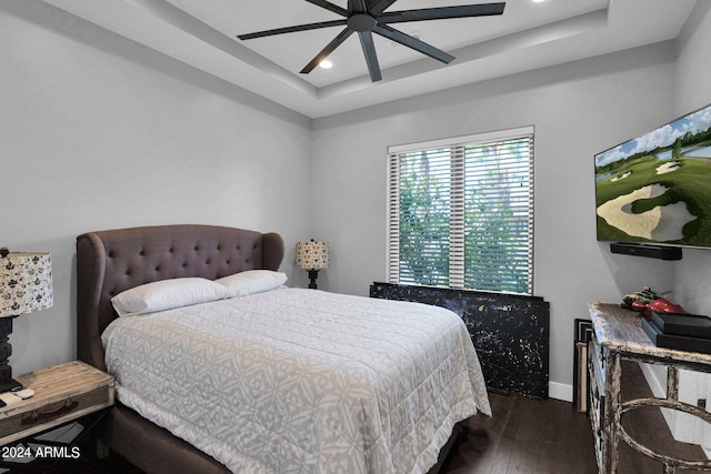 bedroom featuring dark wood-type flooring, a tray ceiling, and ceiling fan