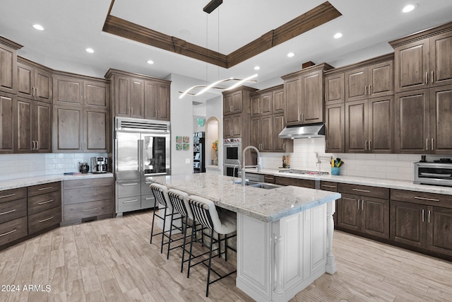 kitchen featuring light stone countertops, appliances with stainless steel finishes, a kitchen island with sink, a kitchen bar, and sink