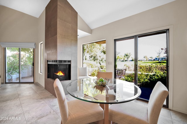 dining room featuring a tile fireplace, plenty of natural light, high vaulted ceiling, and light tile patterned floors