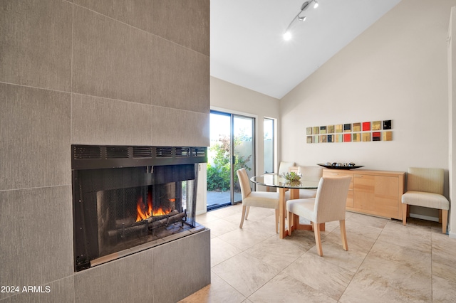 dining area featuring a multi sided fireplace, tile patterned floors, rail lighting, and vaulted ceiling