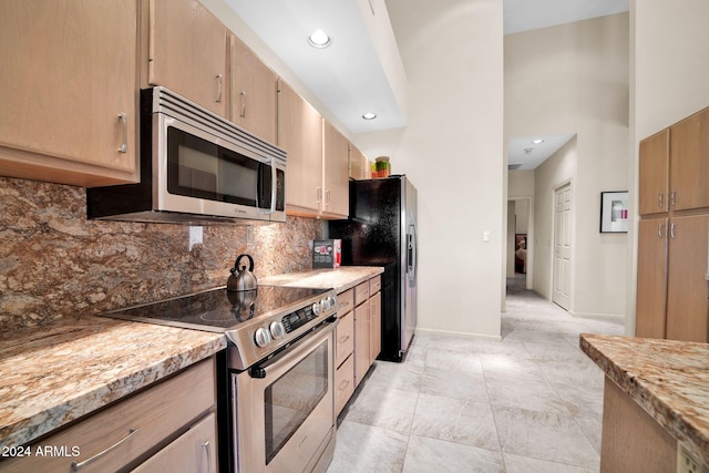 kitchen with decorative backsplash, light brown cabinets, light stone counters, and appliances with stainless steel finishes