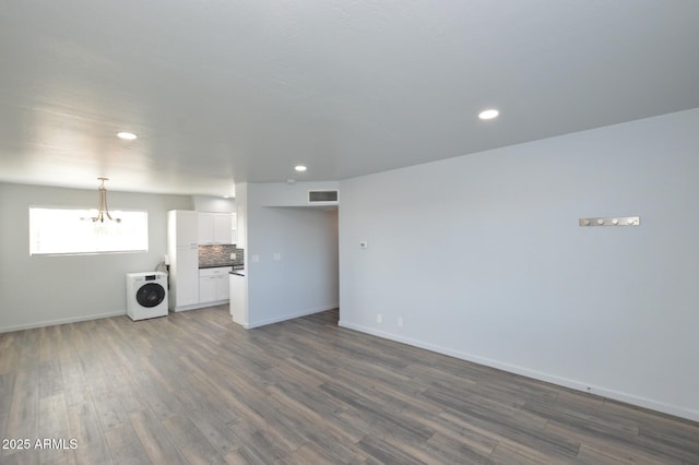 unfurnished living room featuring washer / clothes dryer, dark hardwood / wood-style flooring, and a notable chandelier