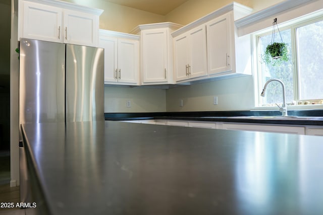 kitchen with dark countertops, white cabinets, a sink, and freestanding refrigerator