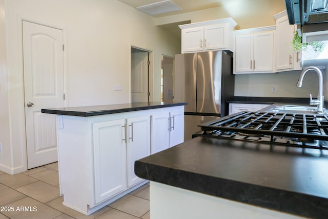 kitchen with light tile patterned floors, dark countertops, a kitchen island, freestanding refrigerator, and white cabinetry