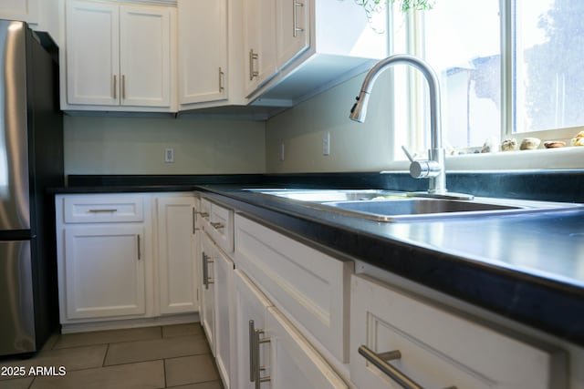 kitchen featuring light tile patterned floors, a sink, freestanding refrigerator, and white cabinetry