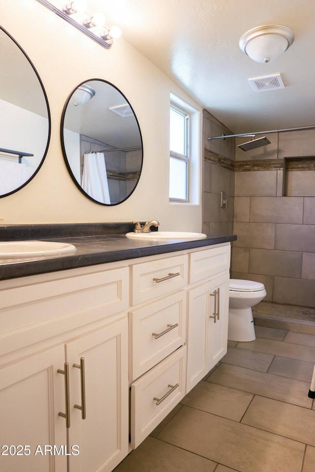 bathroom with toilet, a sink, visible vents, tiled shower, and double vanity