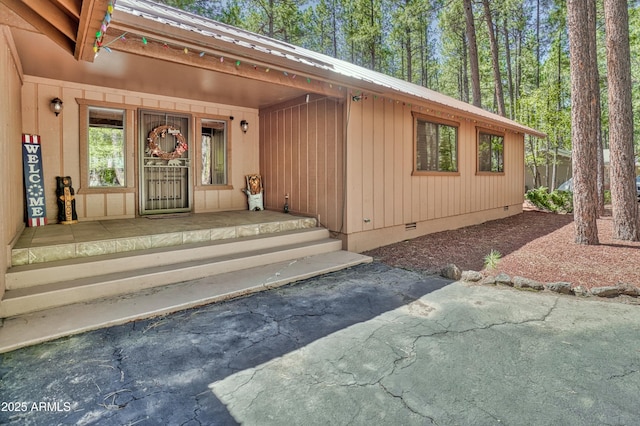 view of exterior entry featuring crawl space, covered porch, and metal roof