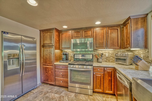 kitchen with light stone counters, recessed lighting, appliances with stainless steel finishes, brown cabinets, and tasteful backsplash