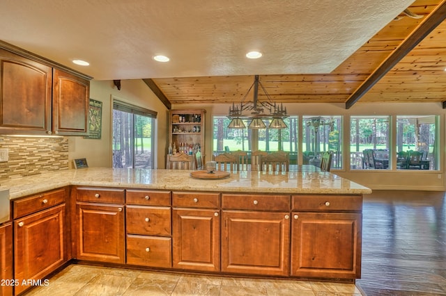 kitchen featuring lofted ceiling, backsplash, light stone countertops, wooden ceiling, and a peninsula