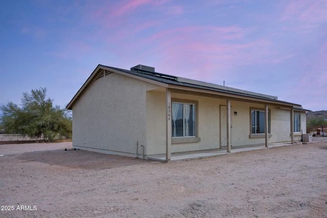 back of property at dusk featuring stucco siding and roof mounted solar panels