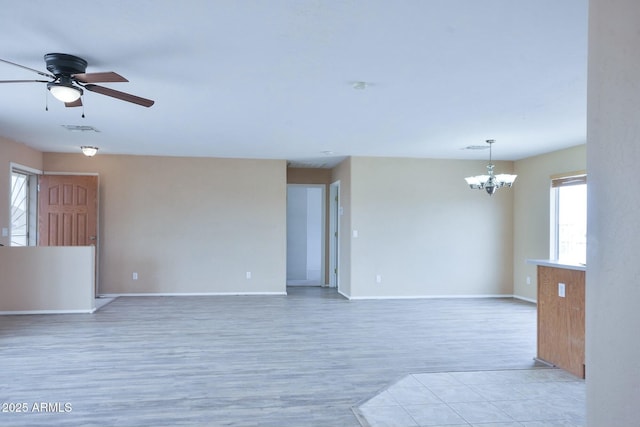 empty room featuring light wood-style floors, baseboards, visible vents, and ceiling fan with notable chandelier