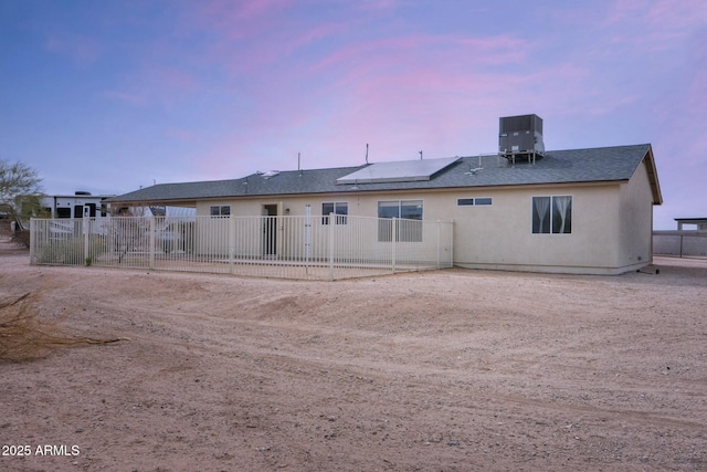 back of property at dusk featuring roof mounted solar panels, fence, and central AC unit