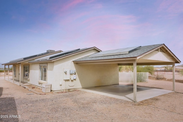 view of front facade with roof with shingles, fence, solar panels, and stucco siding