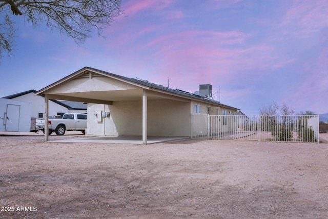 back of property at dusk with central AC, a carport, fence, and stucco siding