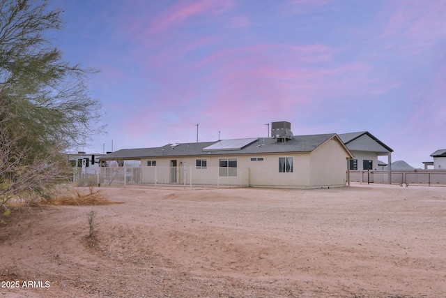 back of house at dusk with central AC unit, fence, and a gate