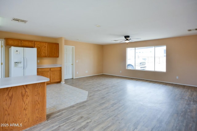 kitchen featuring white fridge with ice dispenser, light countertops, visible vents, and brown cabinets