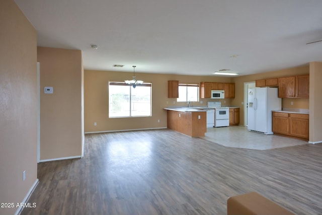 kitchen with white appliances, brown cabinetry, light wood-style flooring, open floor plan, and light countertops