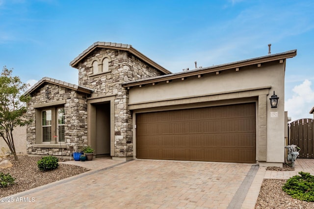 view of front facade featuring a garage, stone siding, decorative driveway, and stucco siding