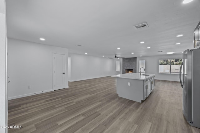 kitchen with hardwood / wood-style floors, sink, a large fireplace, stainless steel refrigerator, and a center island with sink