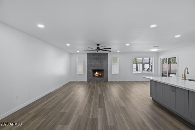 unfurnished living room featuring ceiling fan, dark wood-type flooring, sink, and a tile fireplace