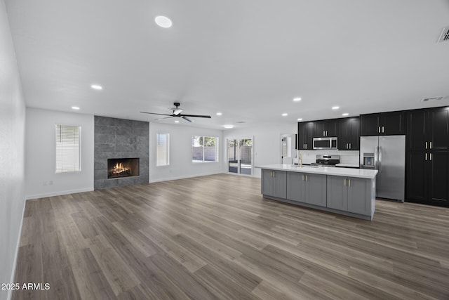 kitchen featuring light hardwood / wood-style floors, a center island with sink, stainless steel appliances, and a fireplace