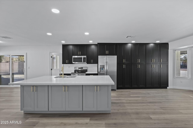 kitchen featuring appliances with stainless steel finishes, a large island with sink, light hardwood / wood-style flooring, and sink