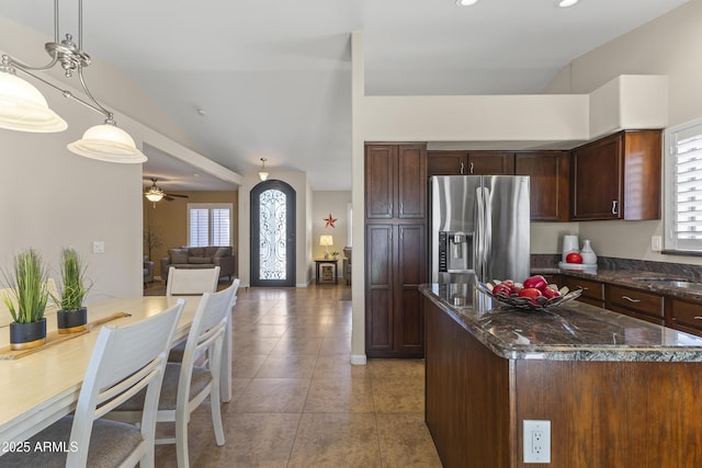 kitchen with stainless steel fridge, light tile patterned flooring, ceiling fan, dark stone countertops, and decorative light fixtures